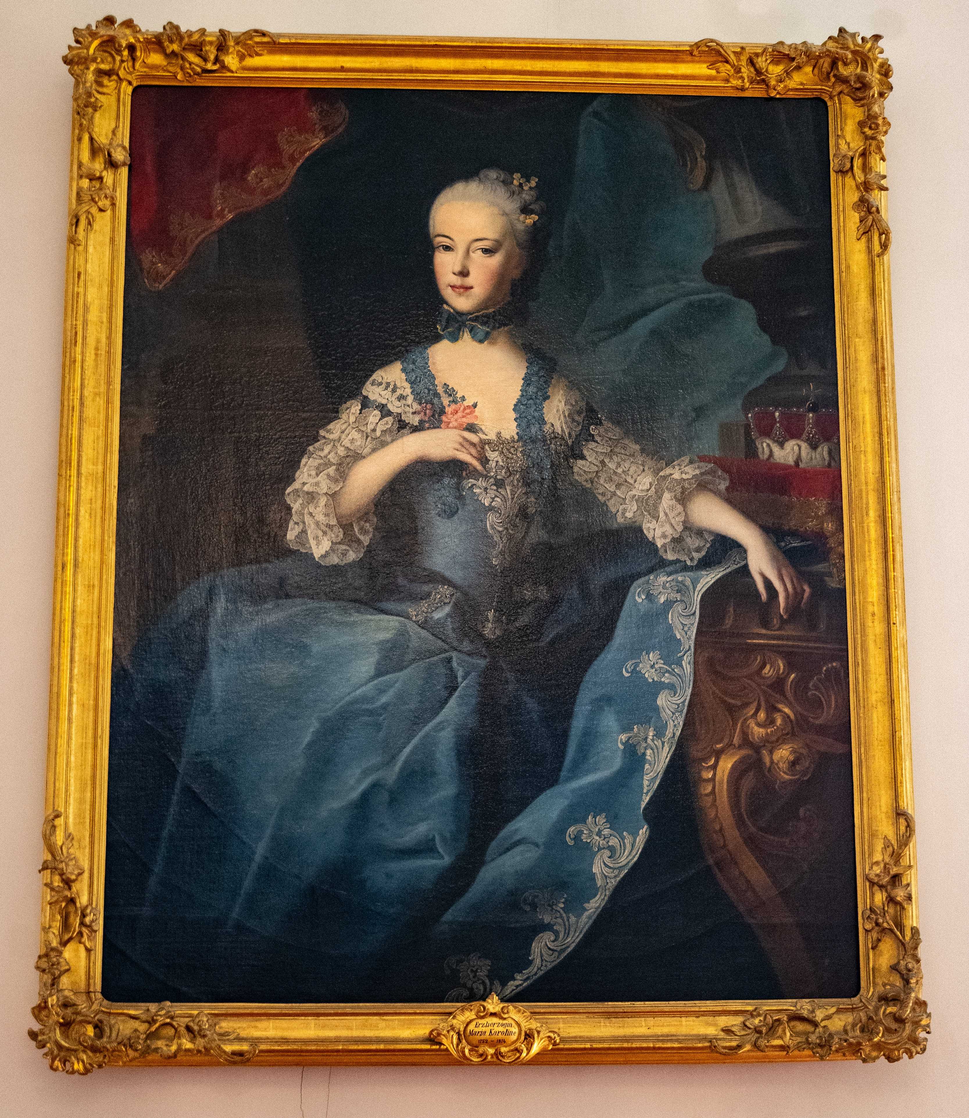 Painting of a woman in a blue dress sitting on a chair.