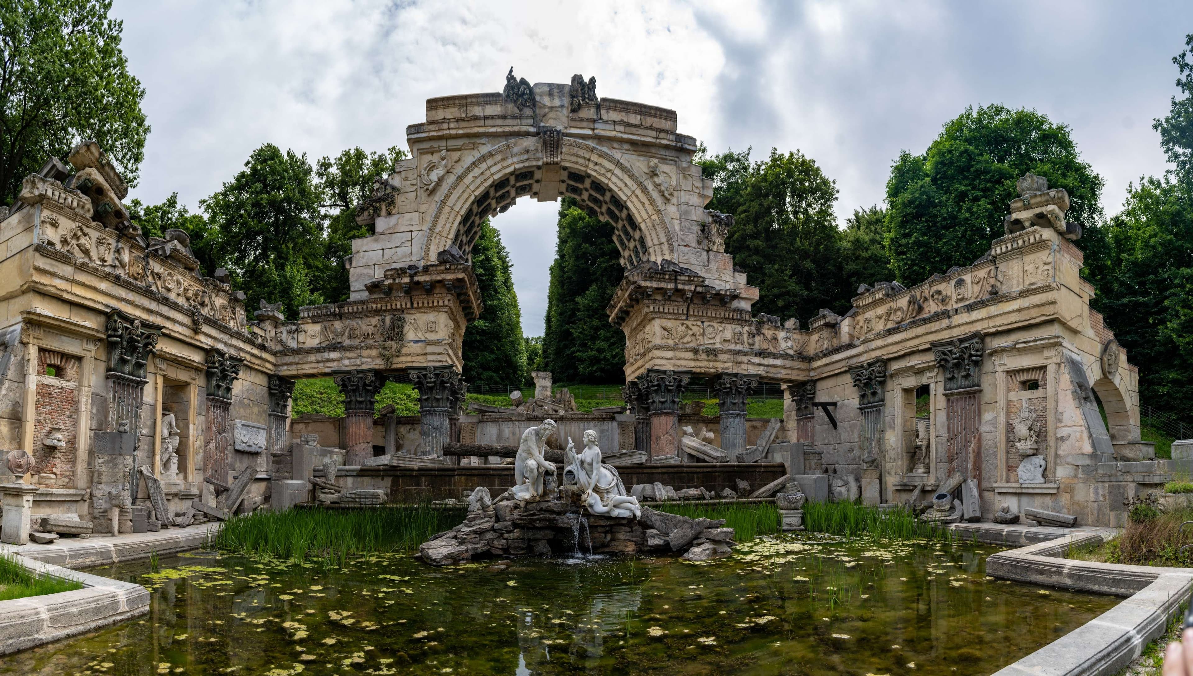 There is a fountain in the middle of a garden with statues.