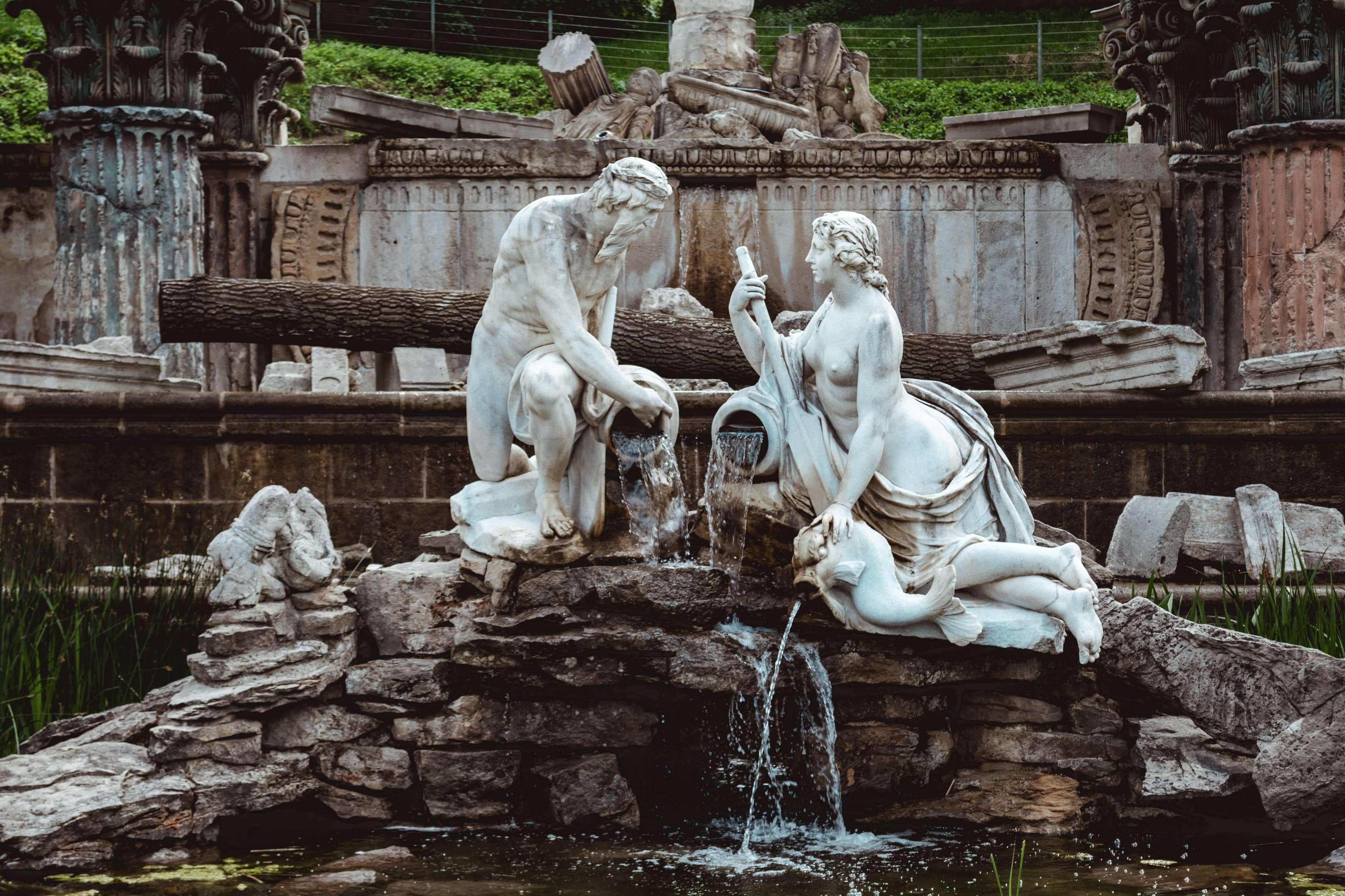 There is a statue of two people sitting on a rock near a fountain.