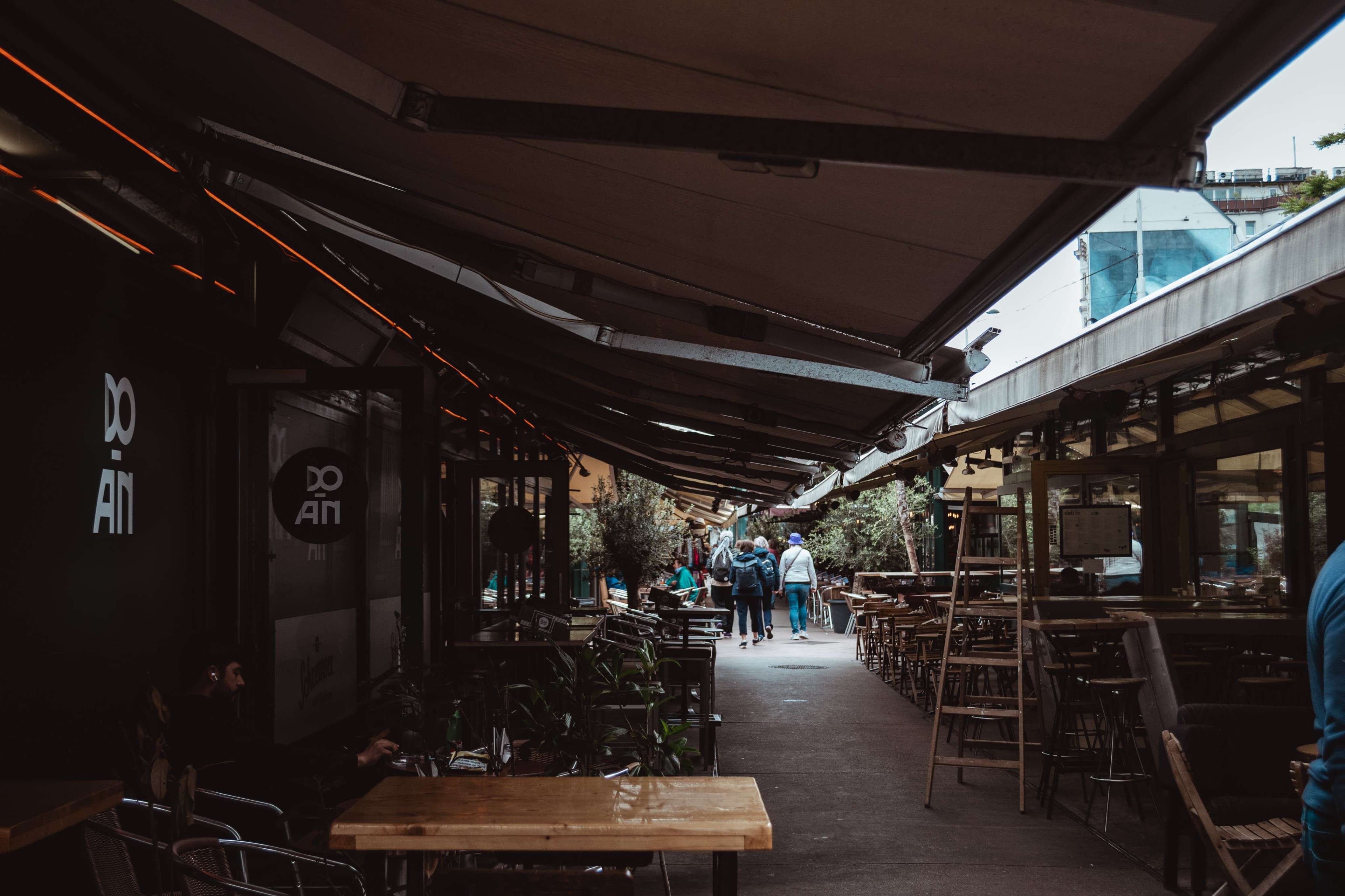 People walking down a sidewalk lined with tables and chairs.