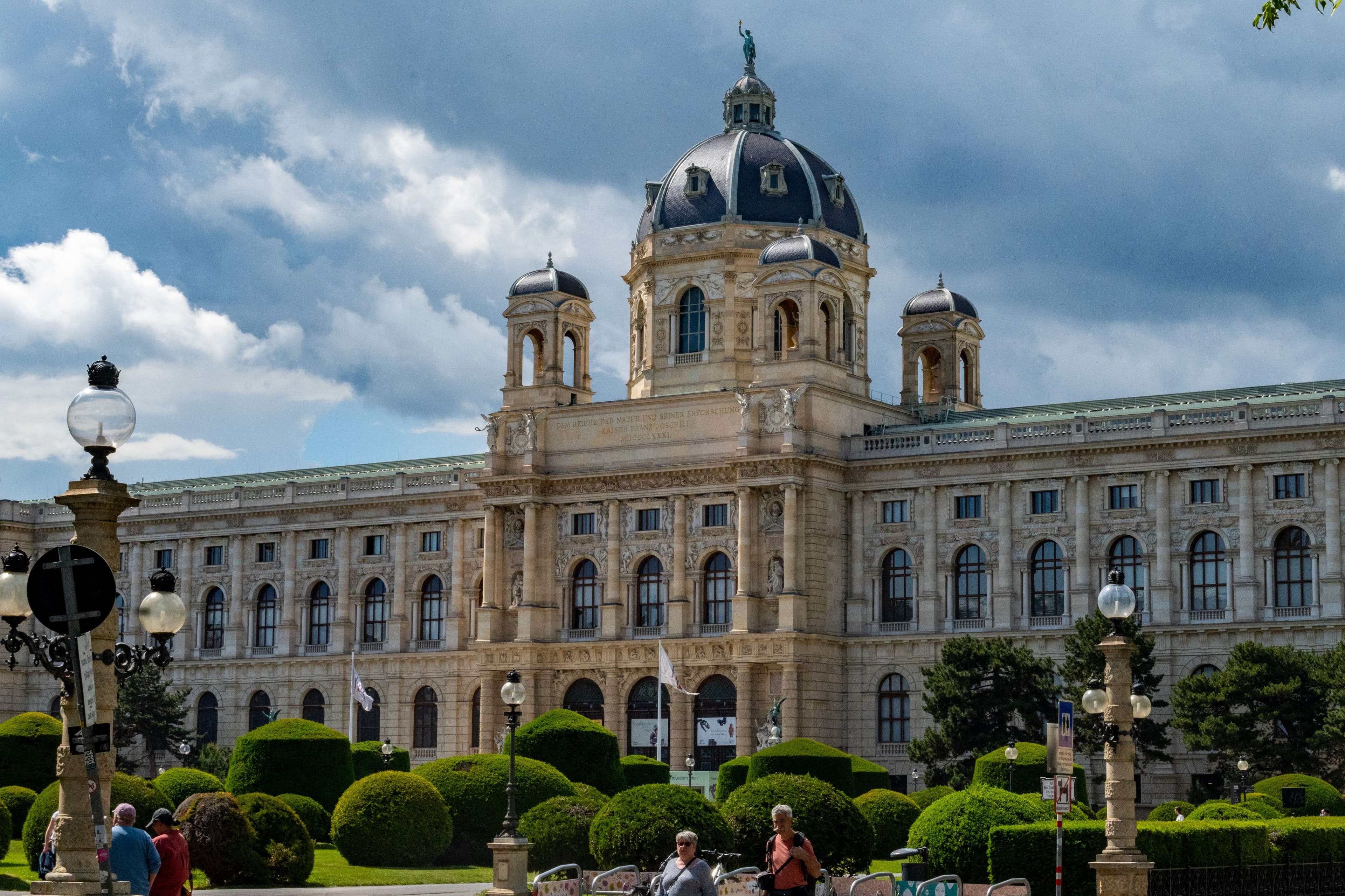 People are walking around in front of a large building with a clock tower.