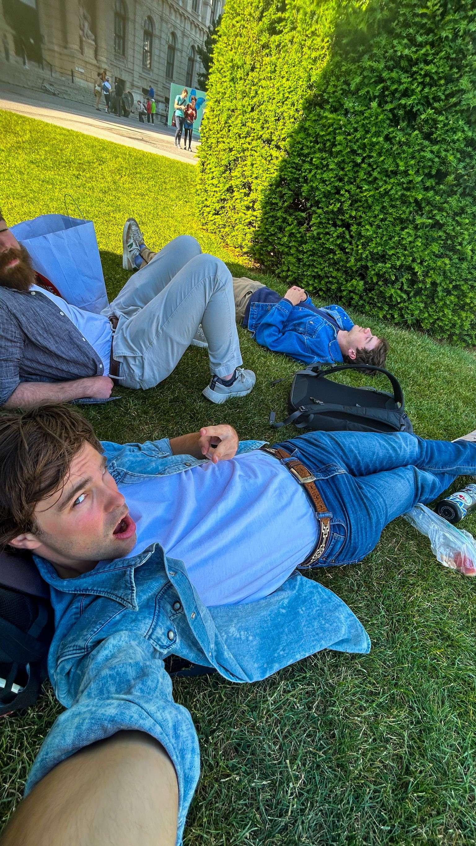 Several people laying on the grass in front of a building.