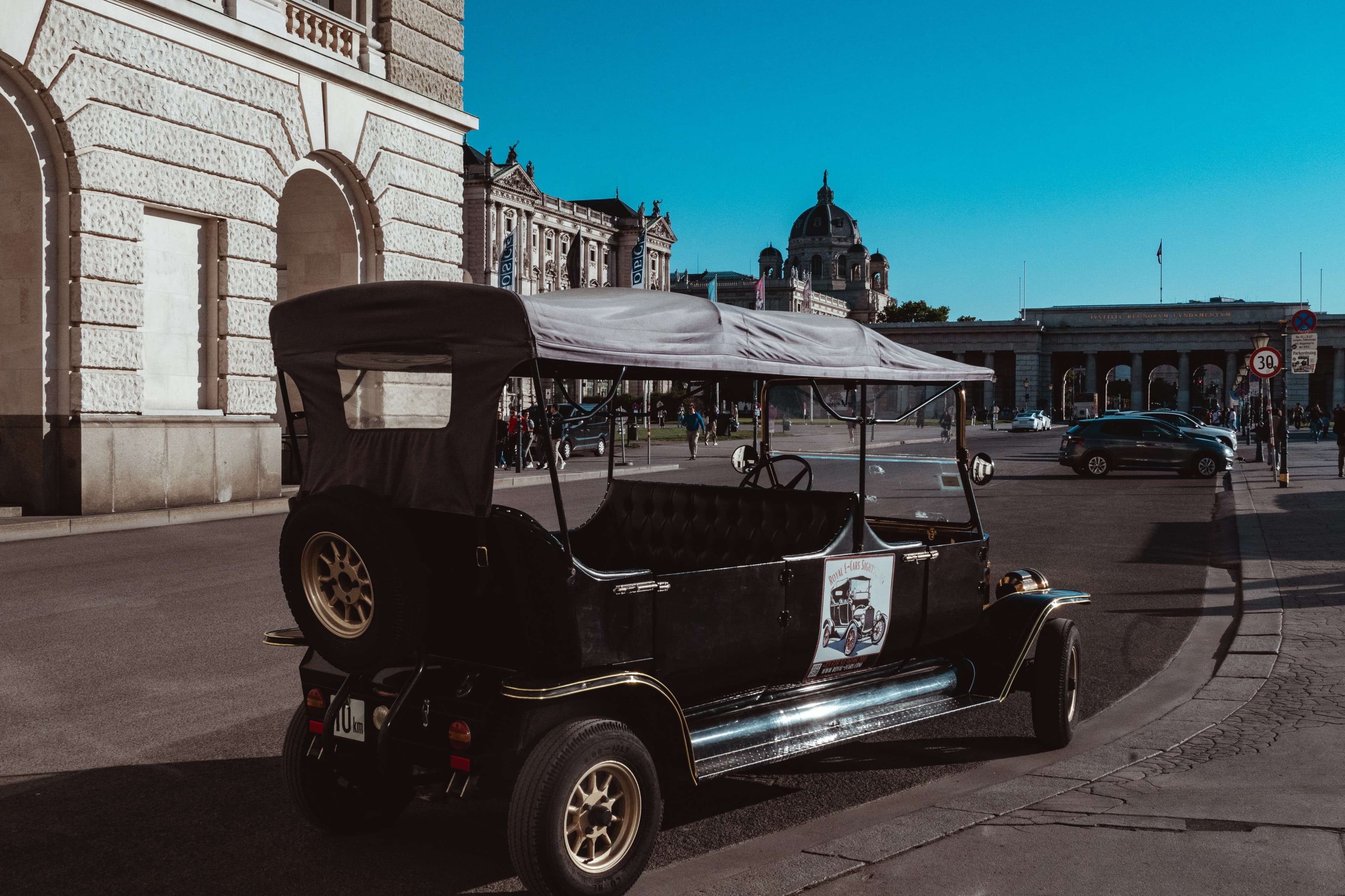 There is a small black car parked on the side of the road.