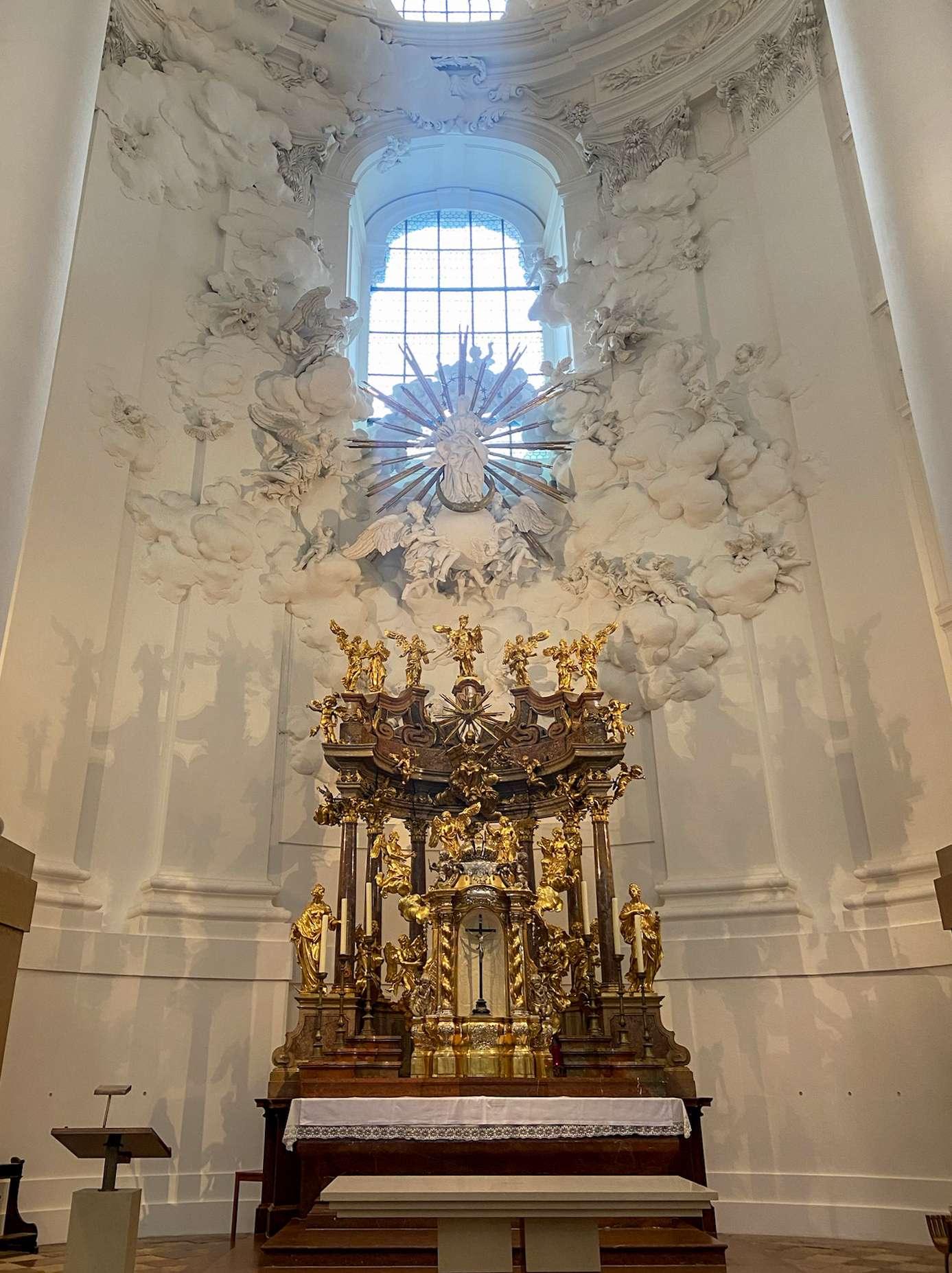 There is a large gold statue in a church with a window.