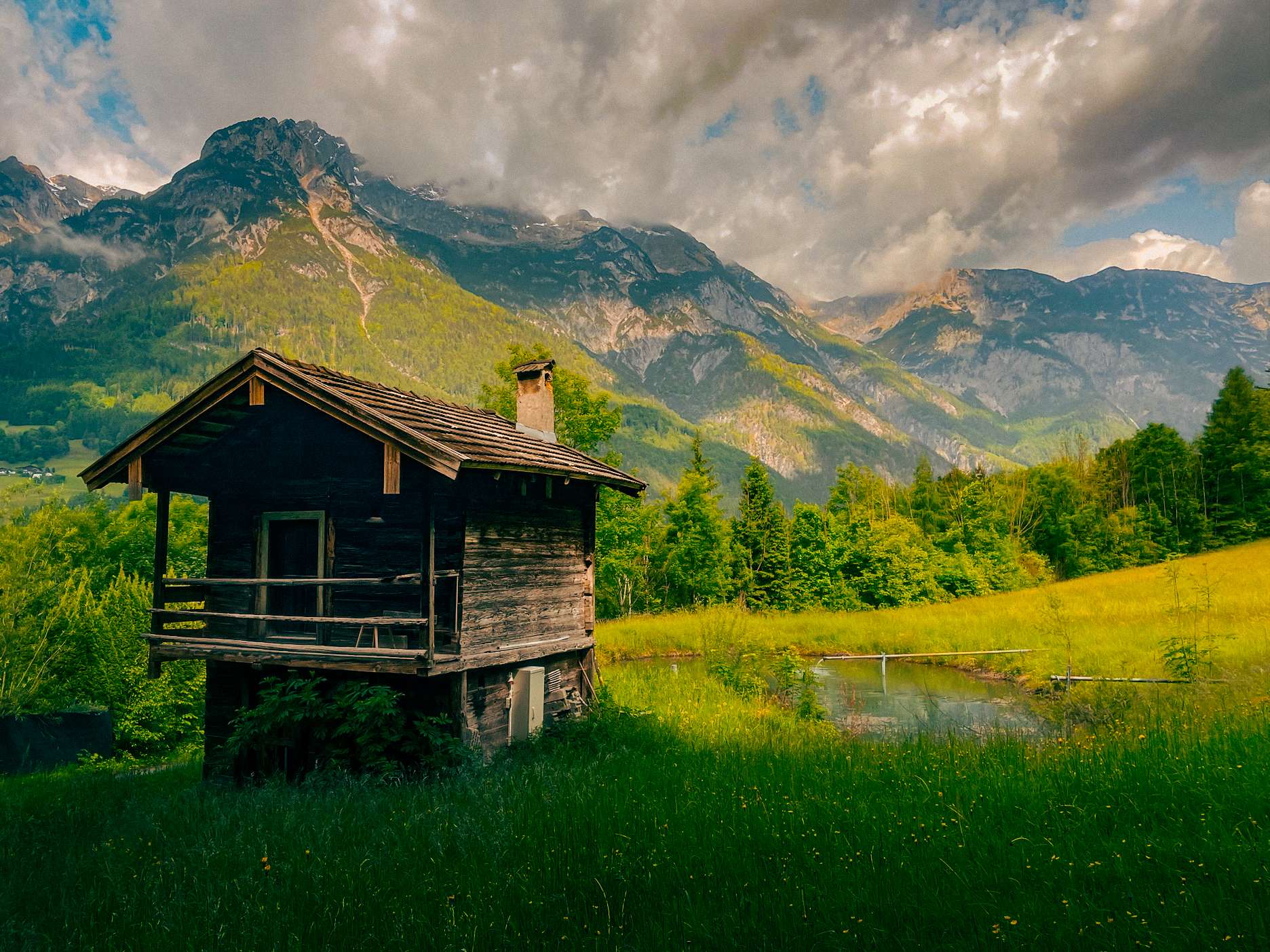 There is a small cabin in the middle of a field with mountains in the background.