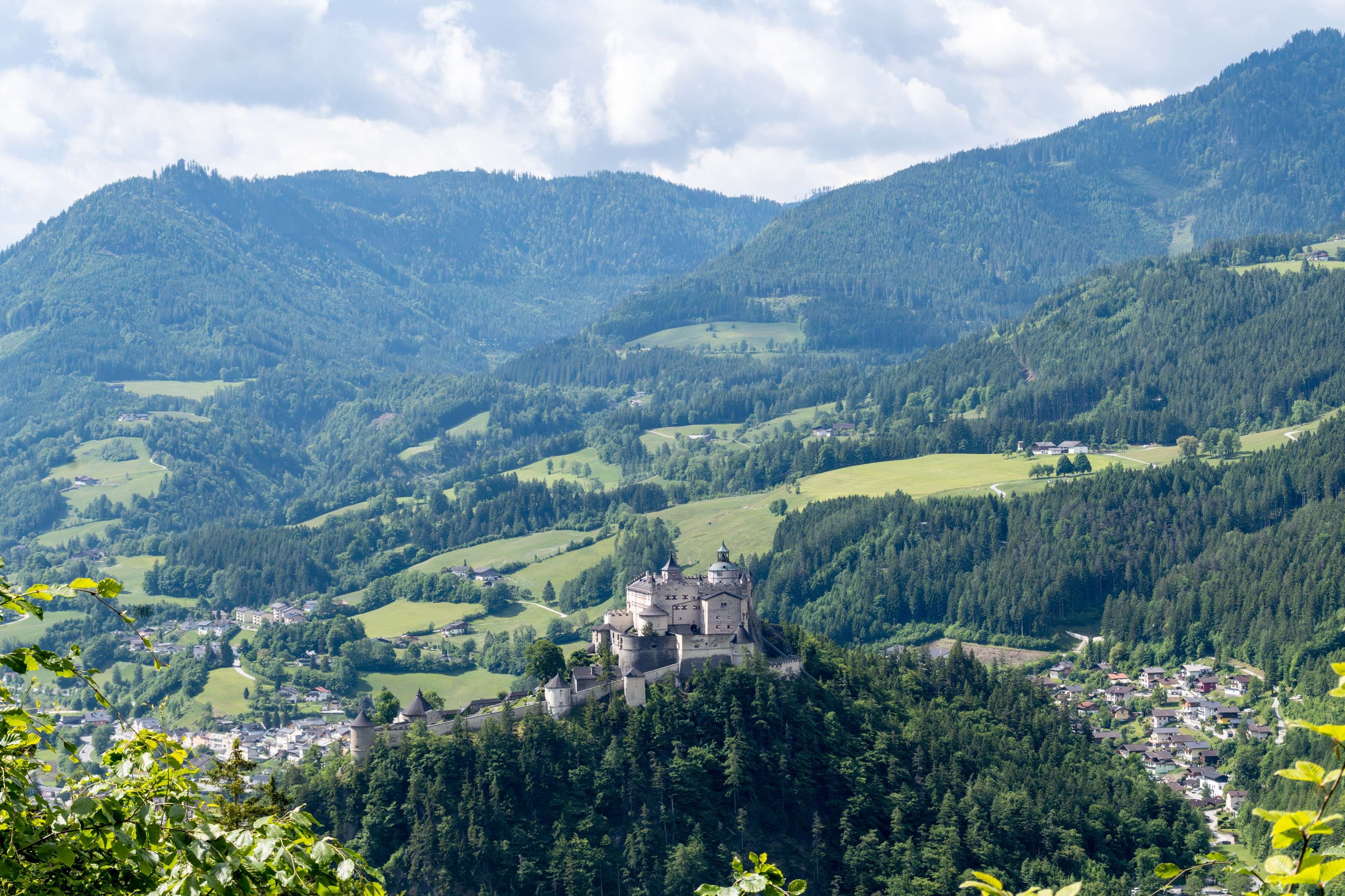 Mountains with a castle on top of it surrounded by trees.