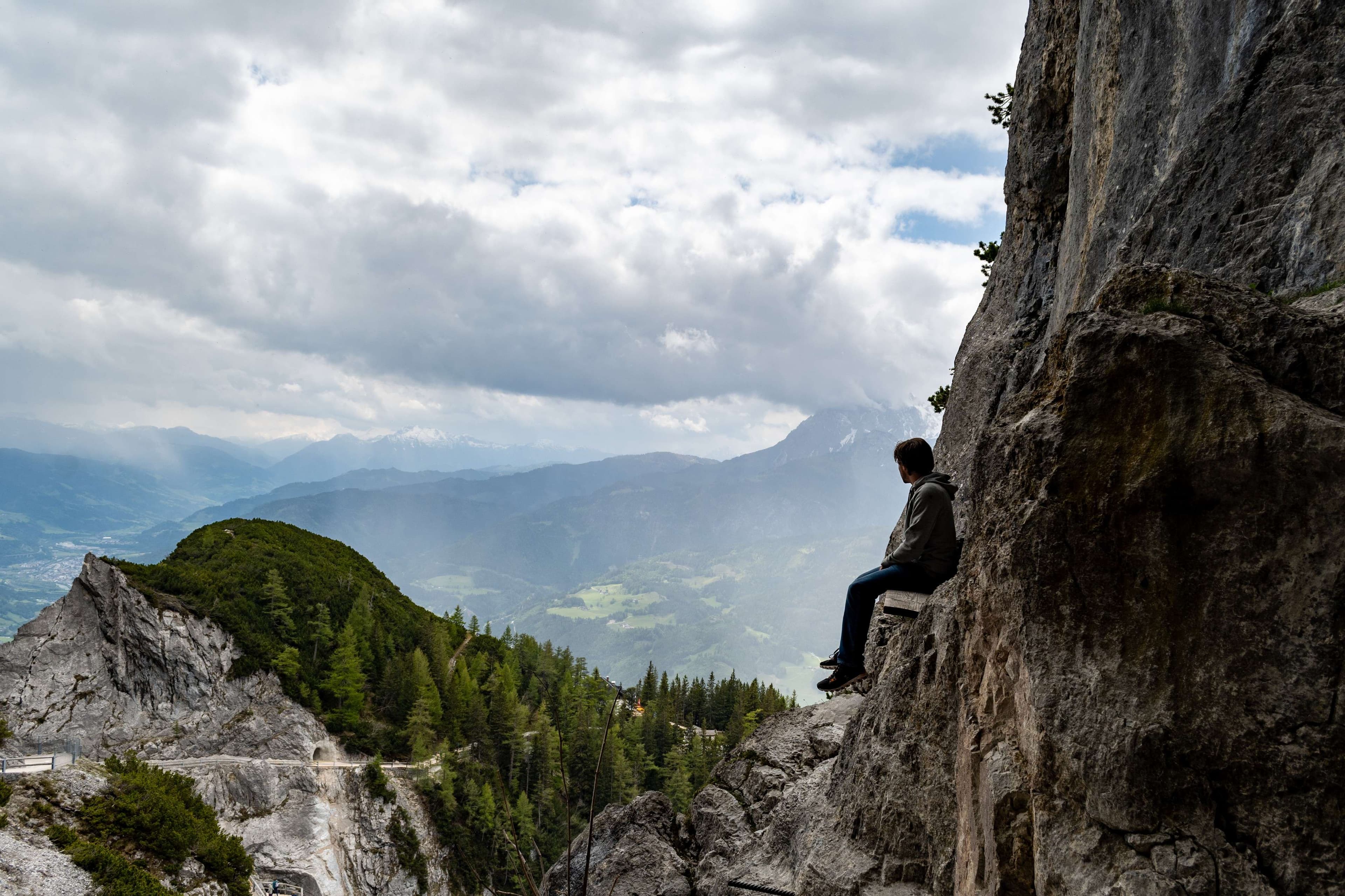 There is a man sitting on a rock on a mountain.