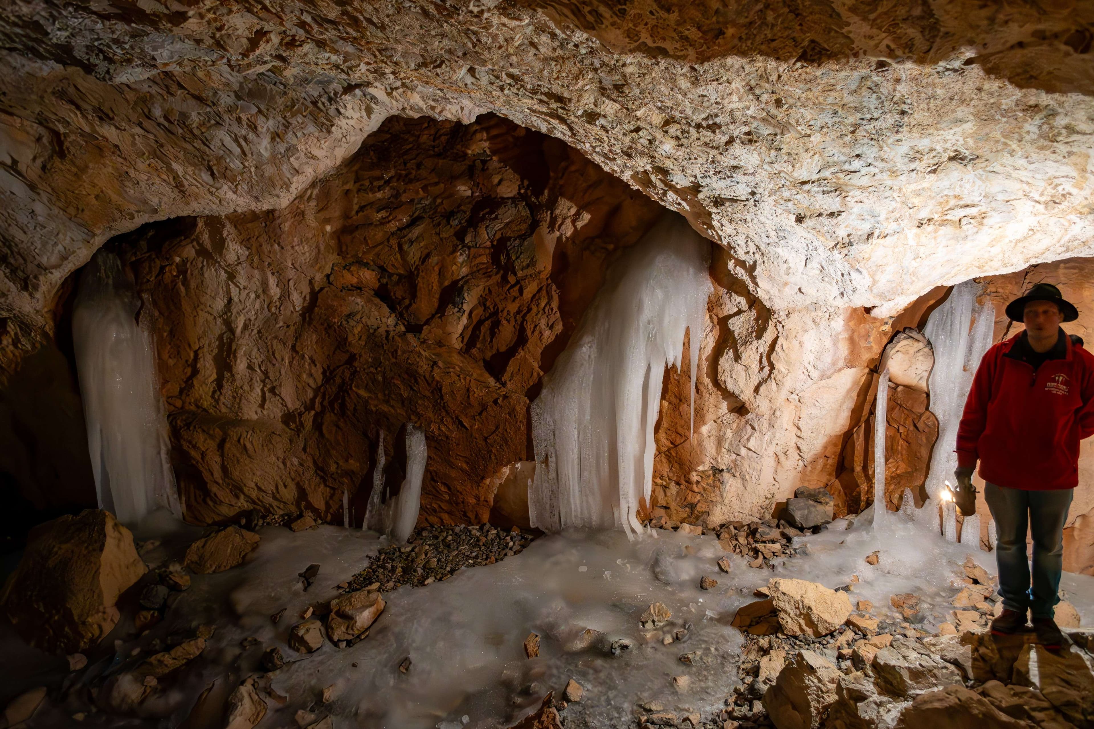 There is a man standing in a cave with ice on the ground.