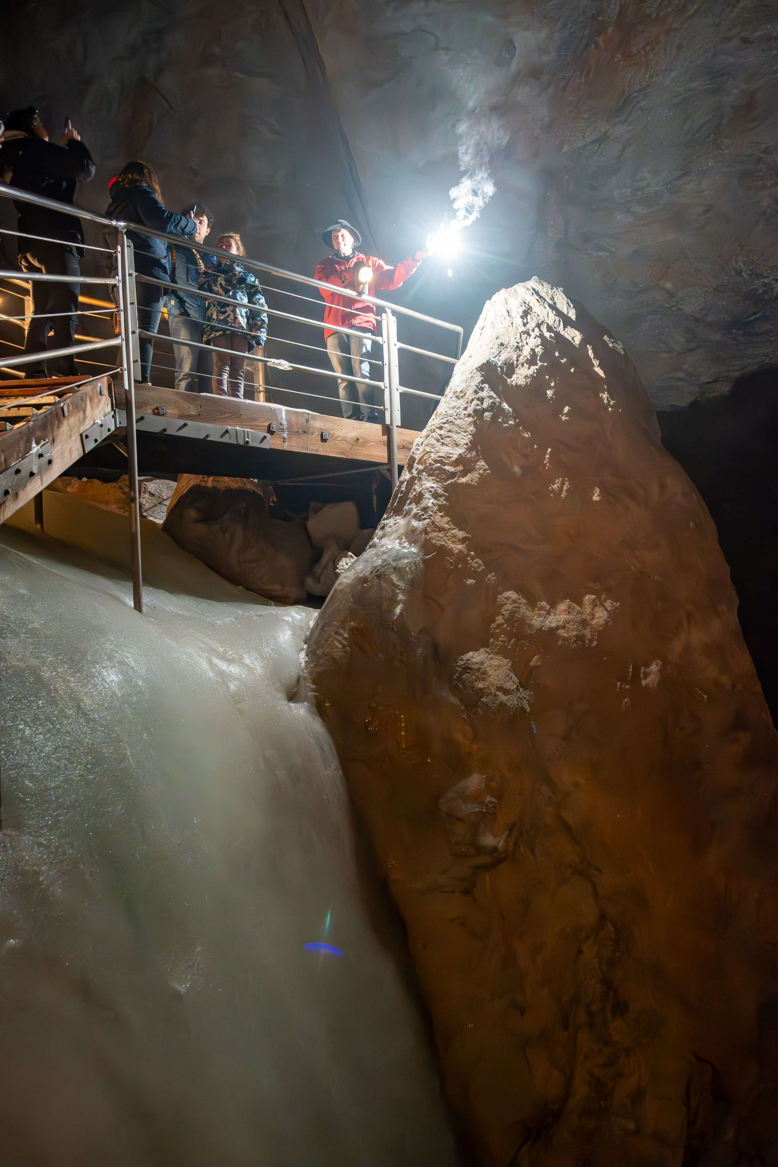 People standing on a bridge in a cave with a light on.