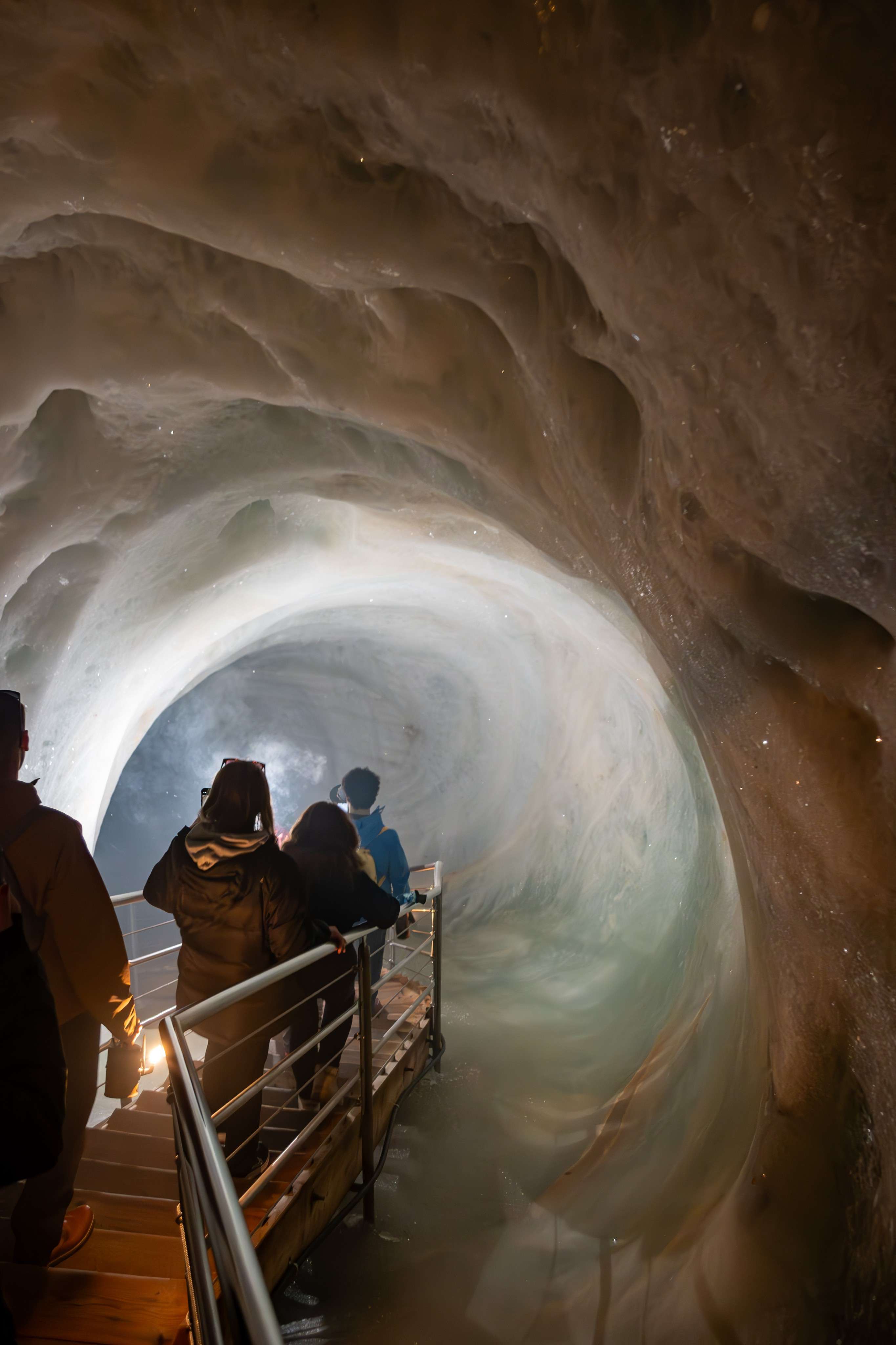 People are walking up a staircase in a cave with a view of the water.