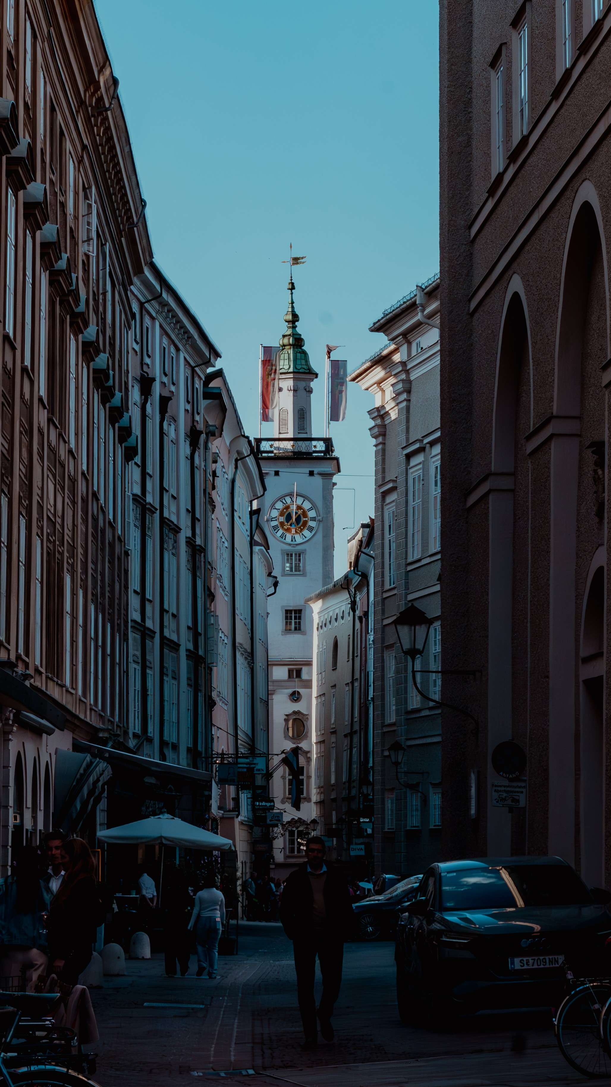 Pedestrians and cars on a city street with a clock tower in the background.