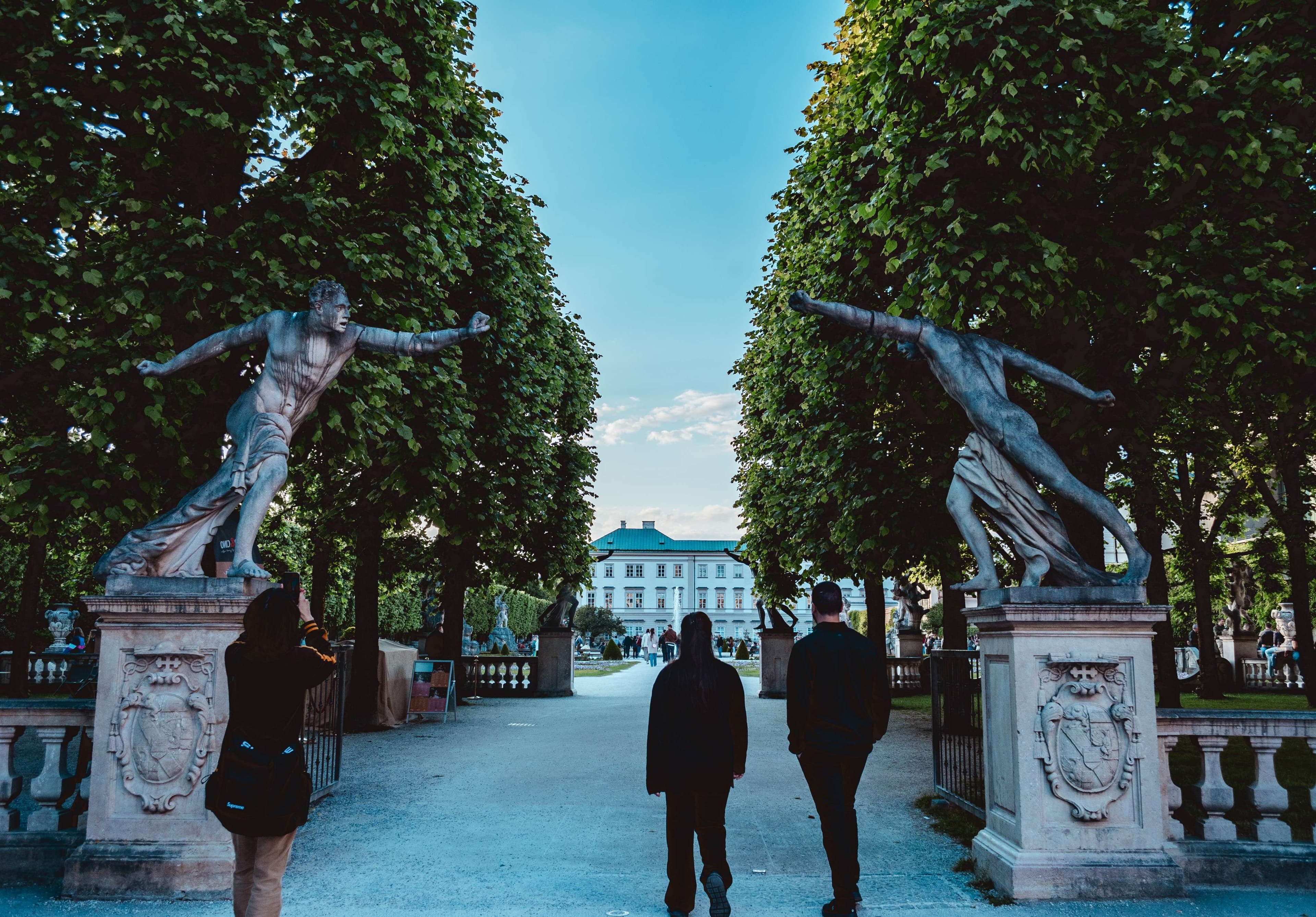There are two people walking down a path between two statues.