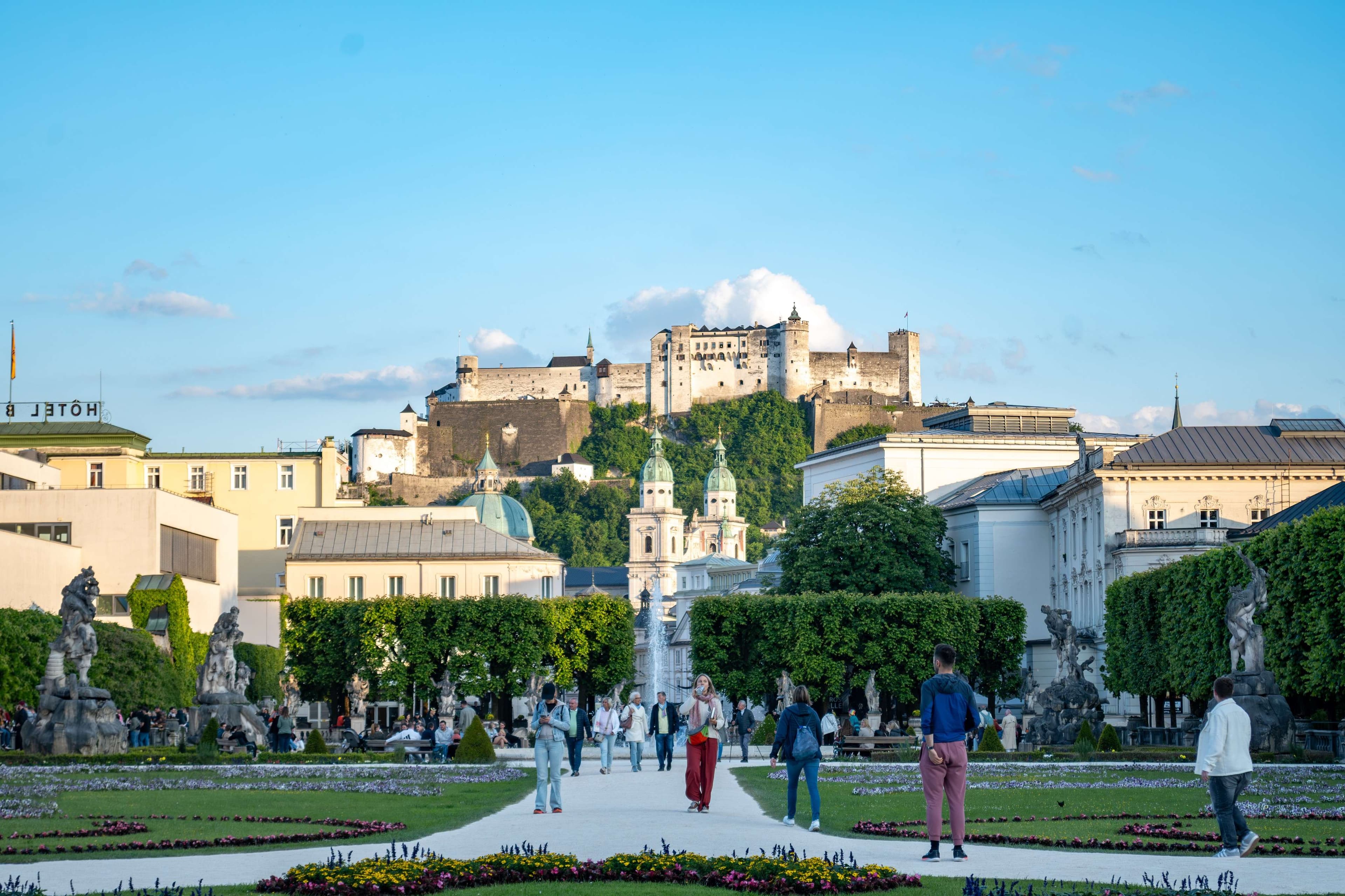 People walking around a park with a fountain in the middle of it.