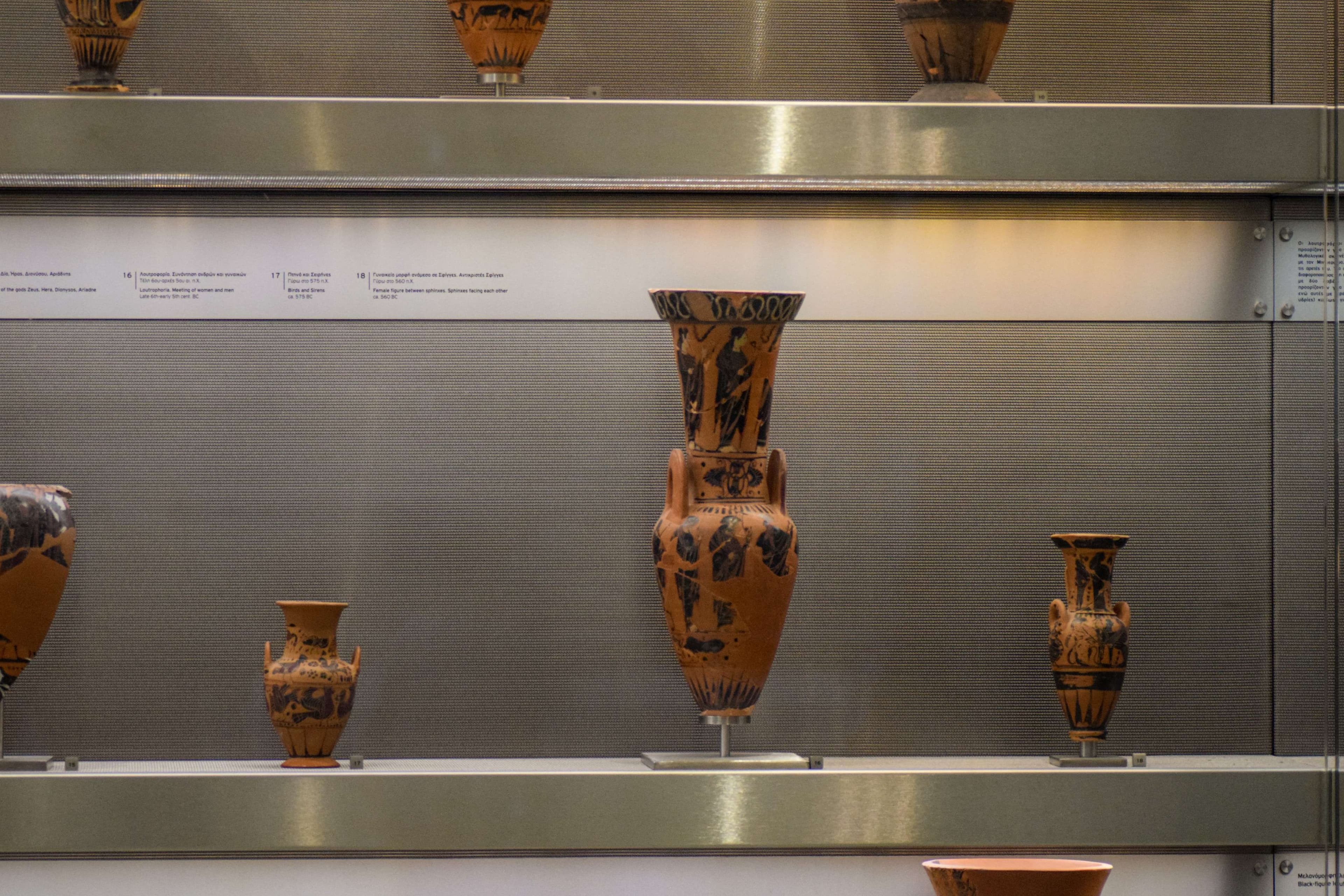 There are many vases on display on the shelf in the museum.