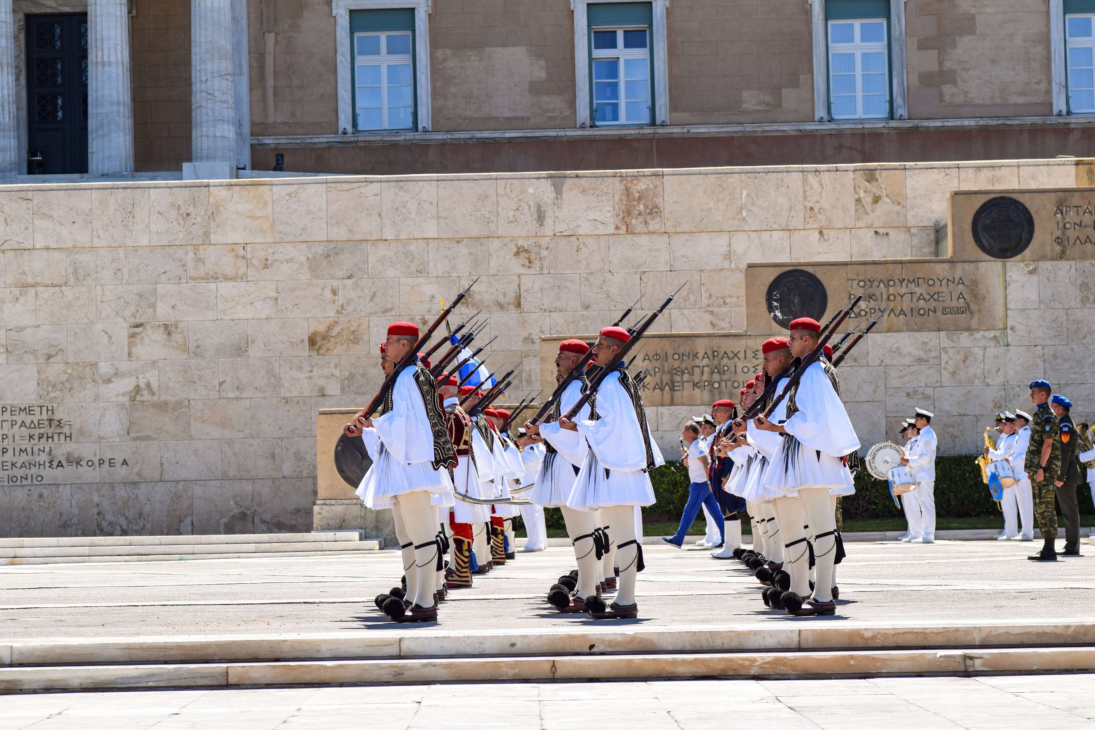 Several soldiers in white uniforms are marching in front of a building.