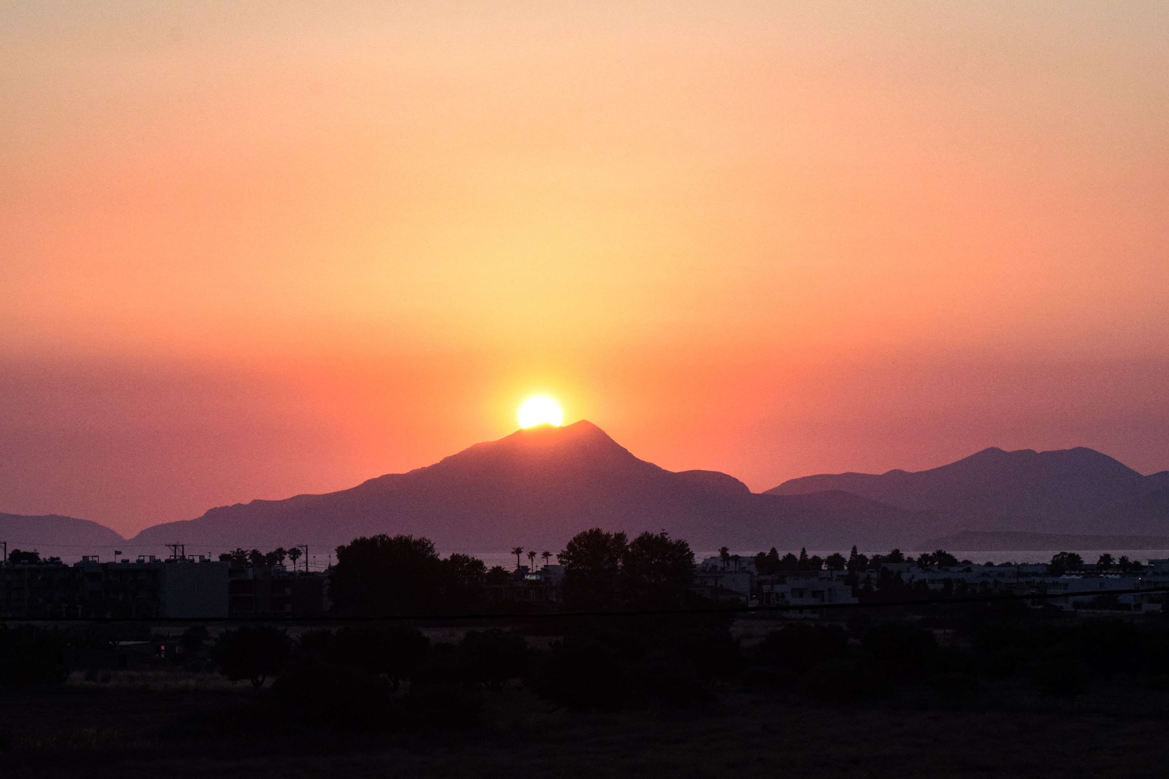Sunset over a mountain range with a plane flying in the sky.