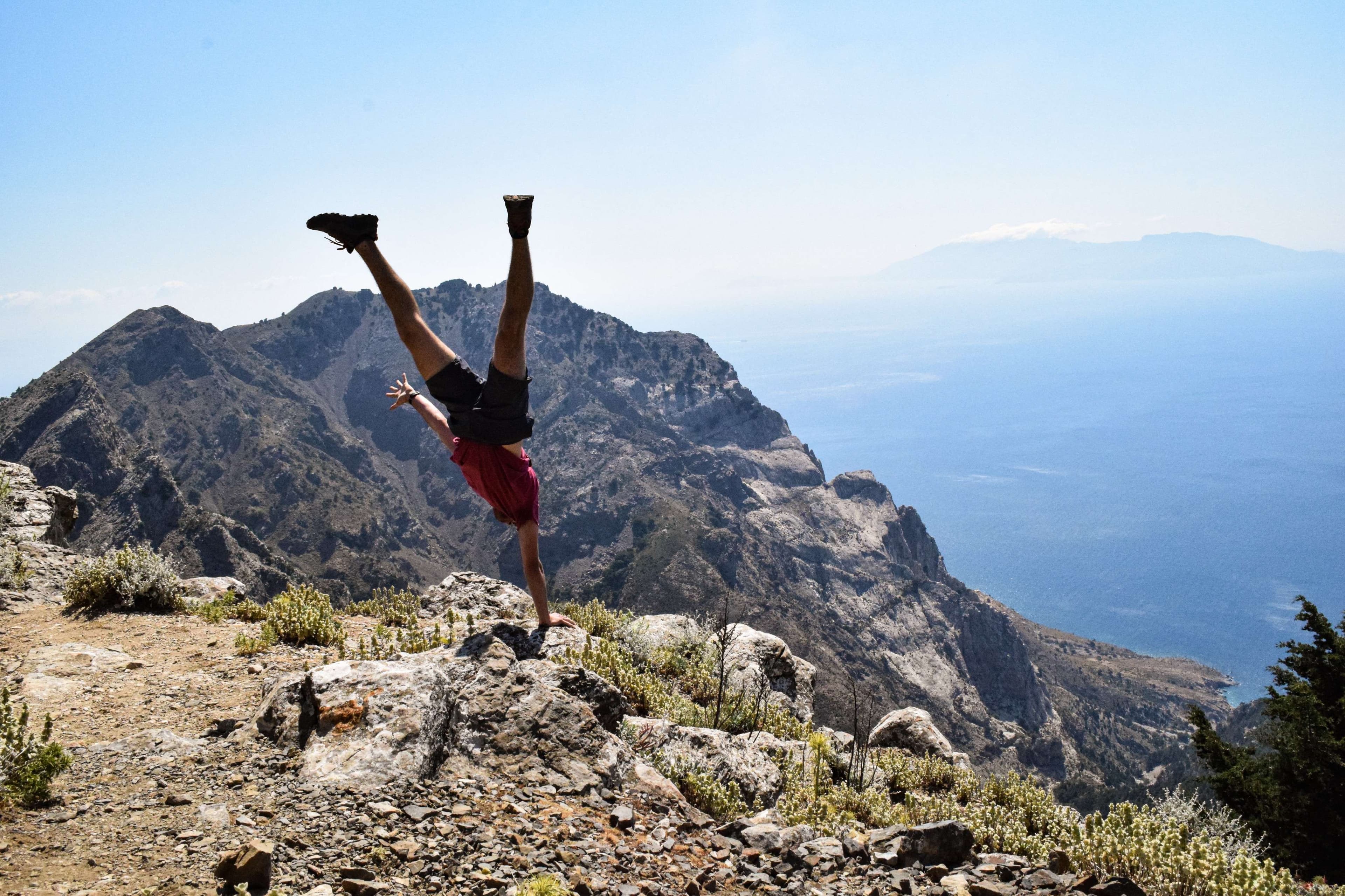 Arafed man doing a handstand on a mountain top.