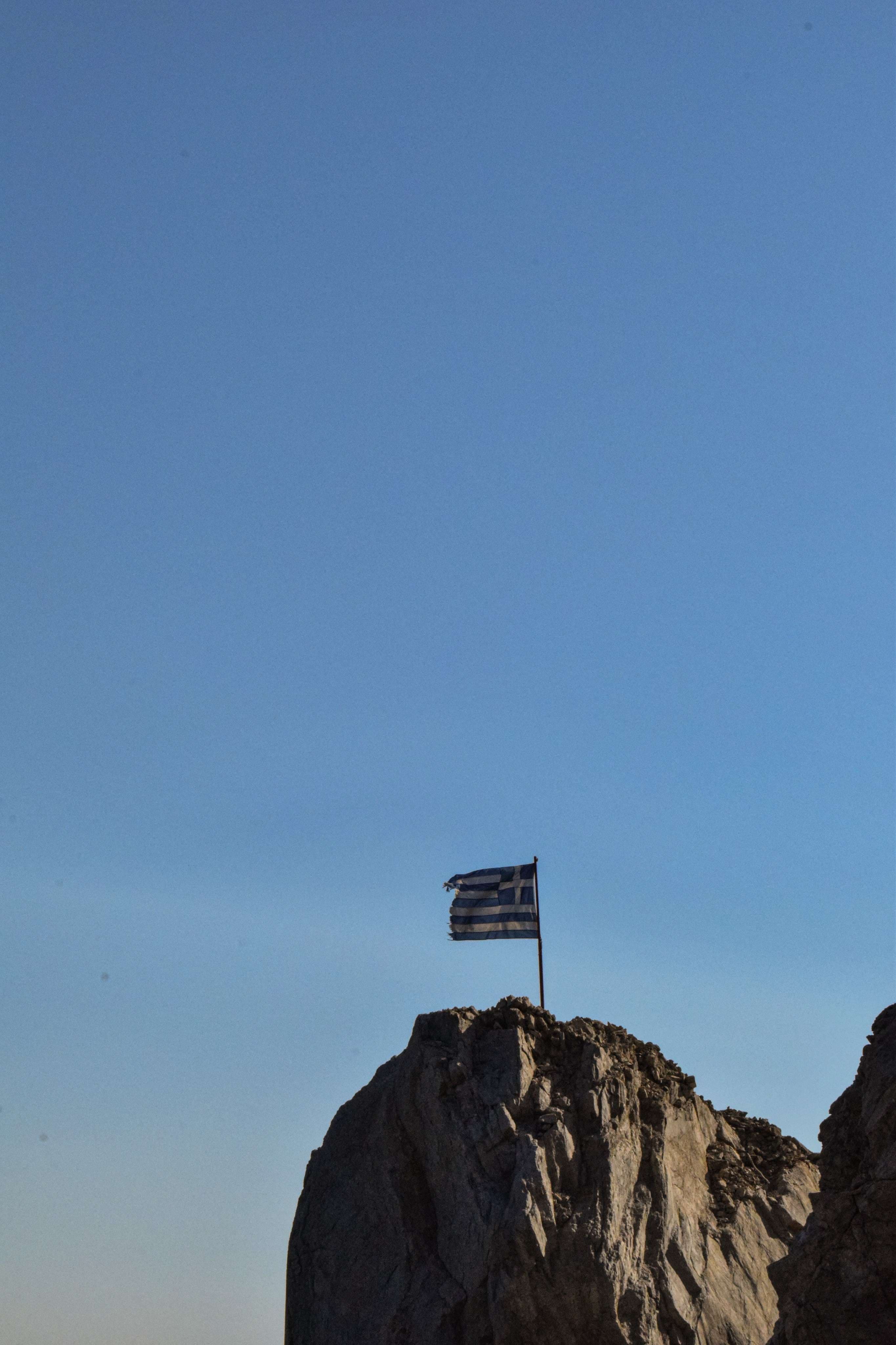 There is a flag on a rock in the middle of the ocean.