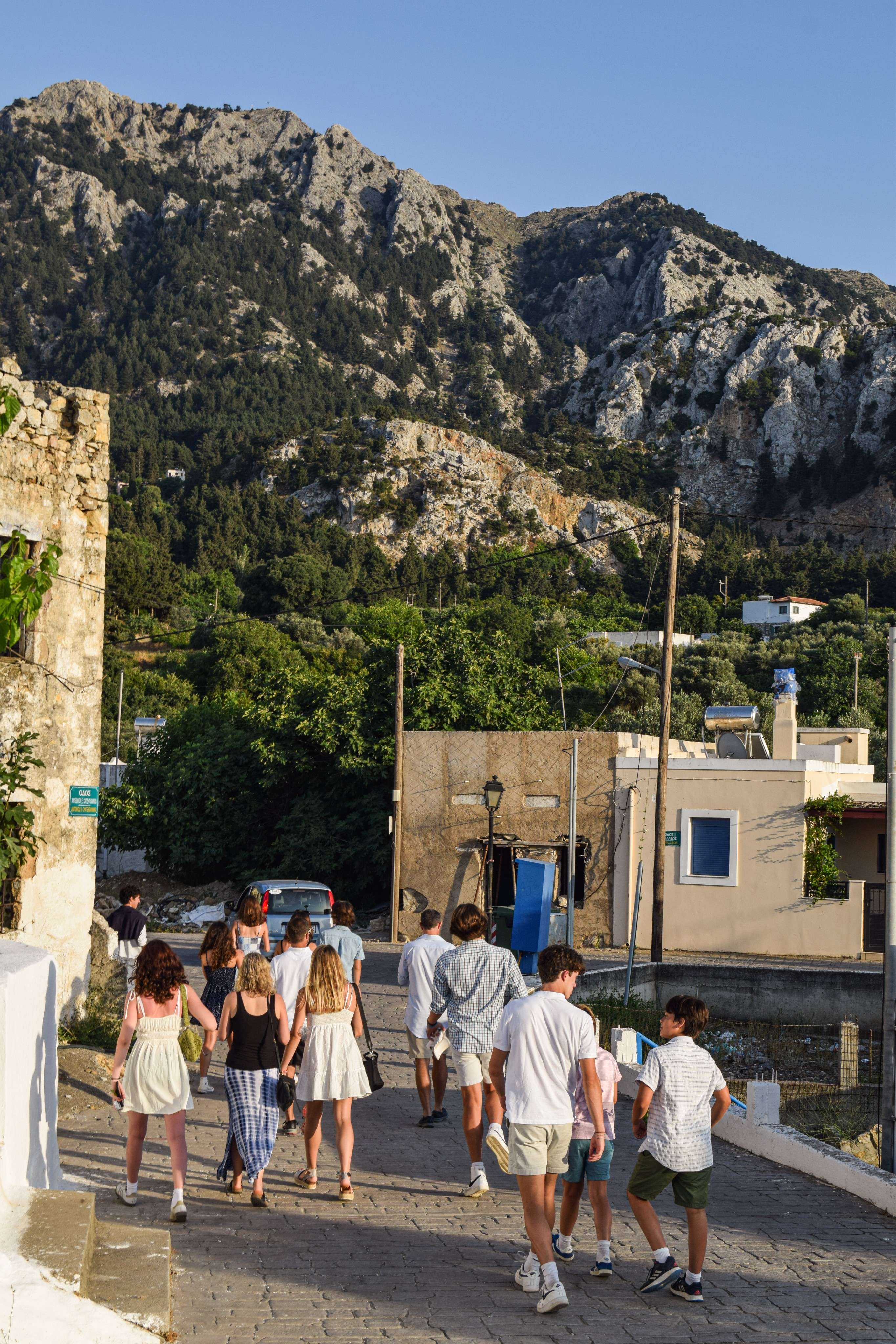 People walking down a street in a village with a mountain in the background.