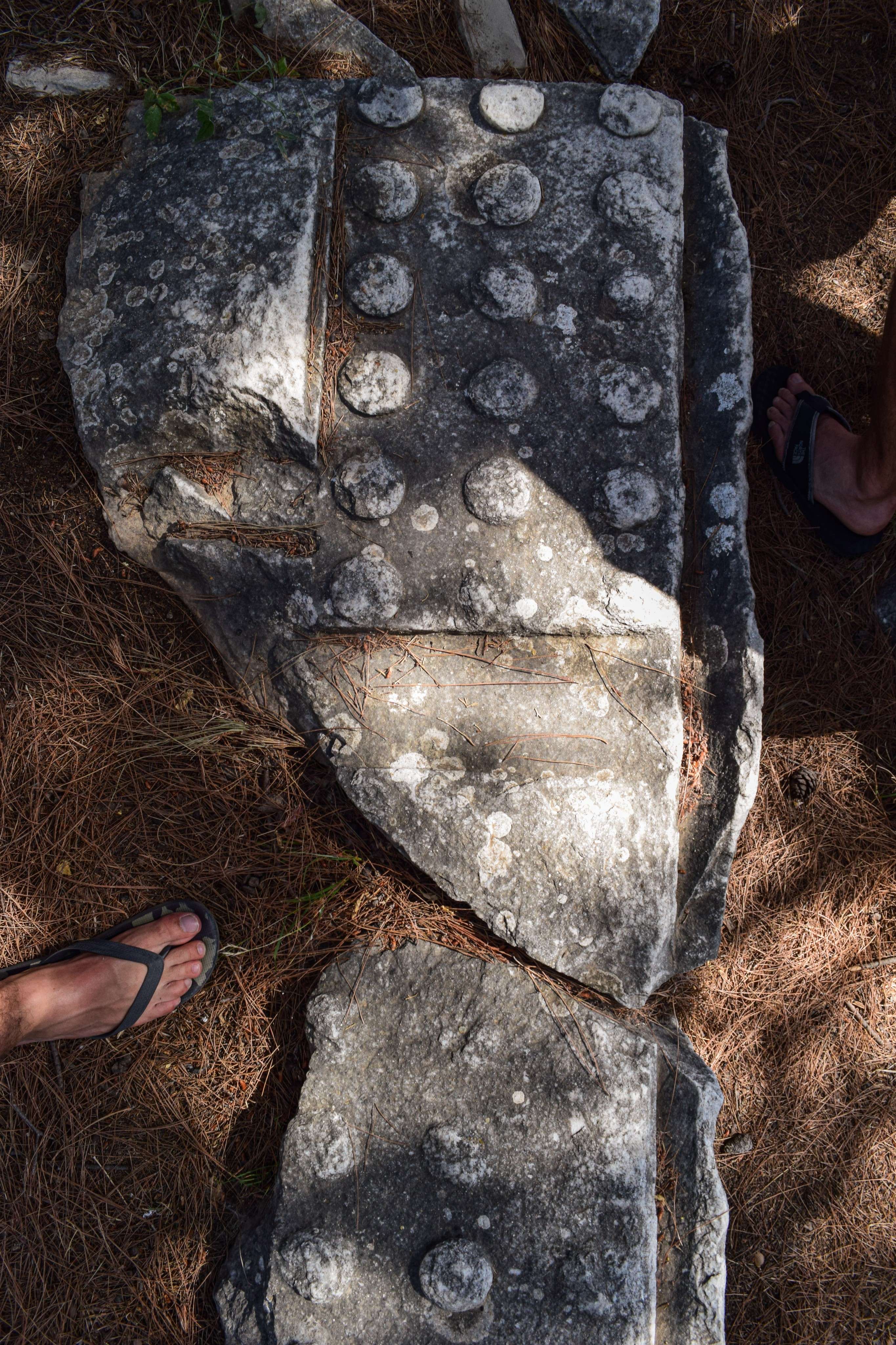 Someone standing next to a large rock with a face on it.