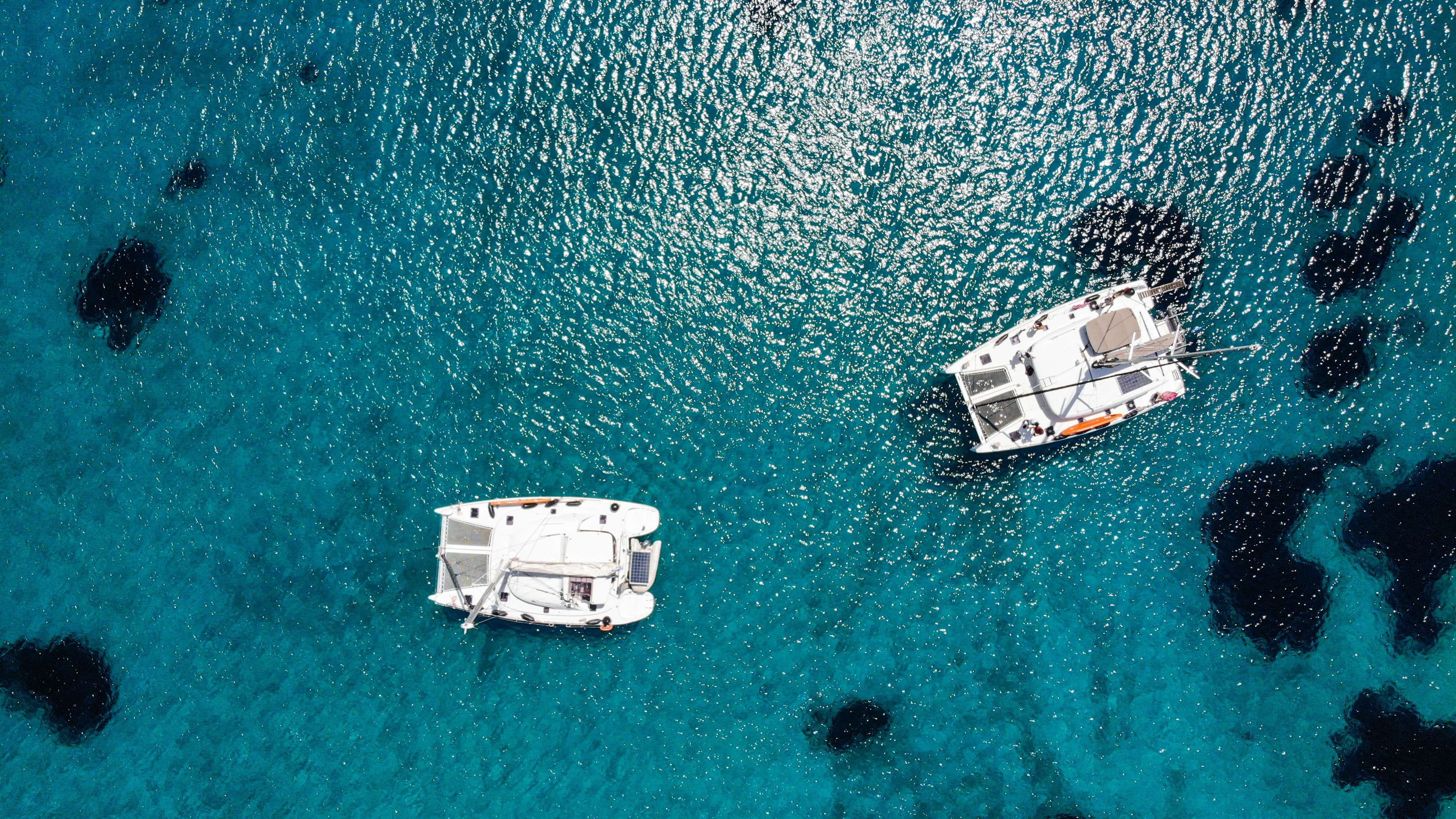 Two boats in the water near a rocky shore with a blue sky.