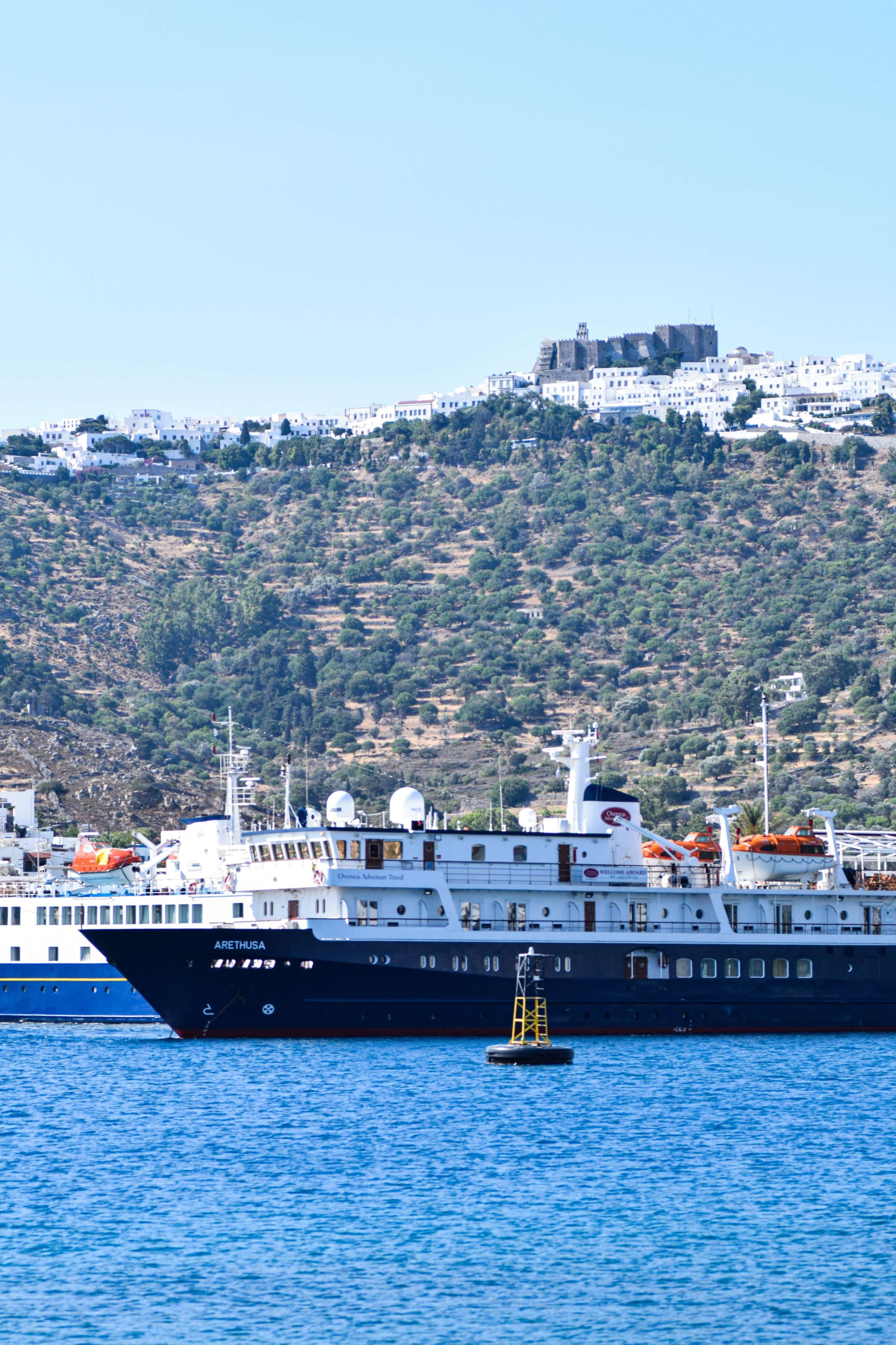 There are two large ships in the water near a hill.