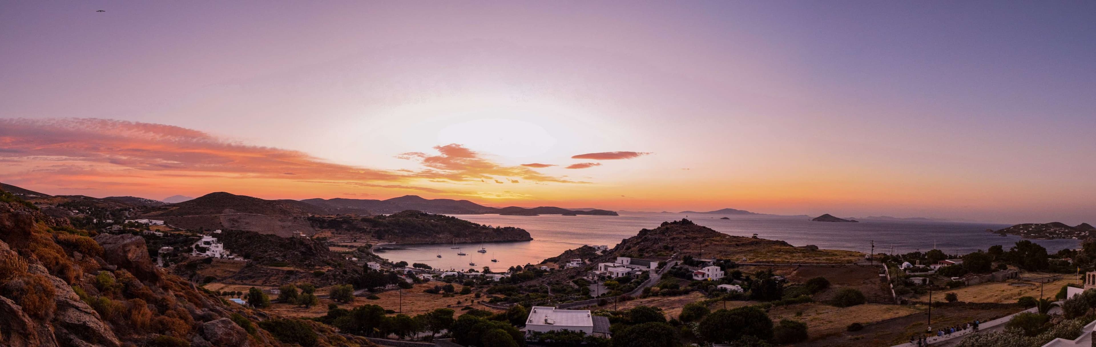 Sunset over a small town with a body of water in the distance.